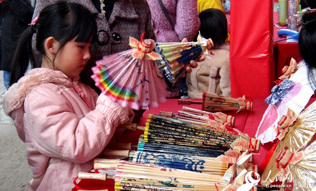  在福州油纸伞的摊位前，一个小朋友对一把卡通小伞爱不释手
